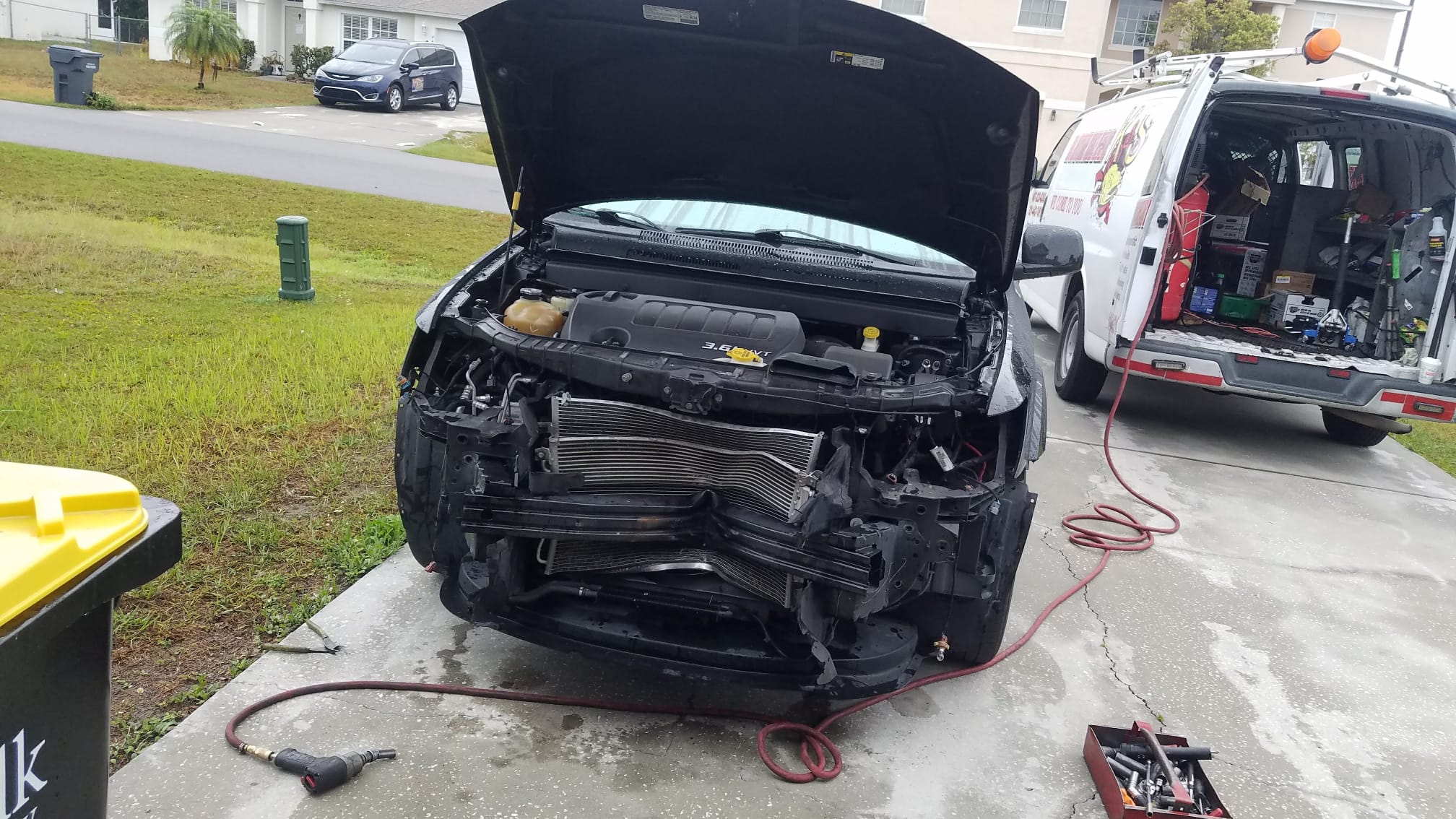 A minivan with the front clip removed, engine exposed, K&S van parked behind