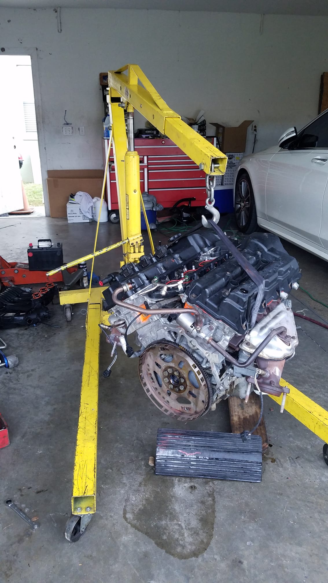 An engine hanging from a yellow engine hoist in a garage