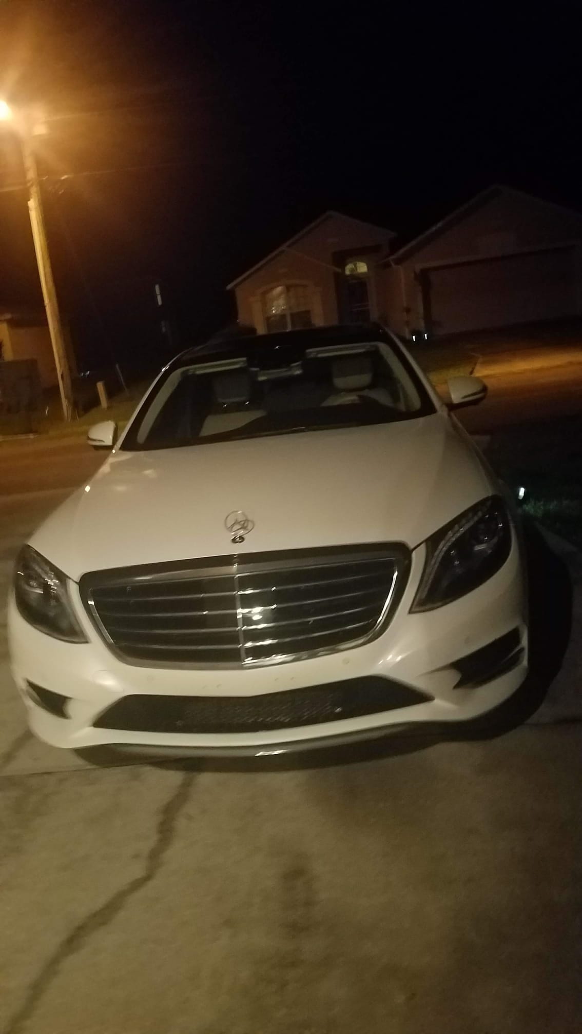A white Mercedes-Benz S-Class parked in a driveway at night after service