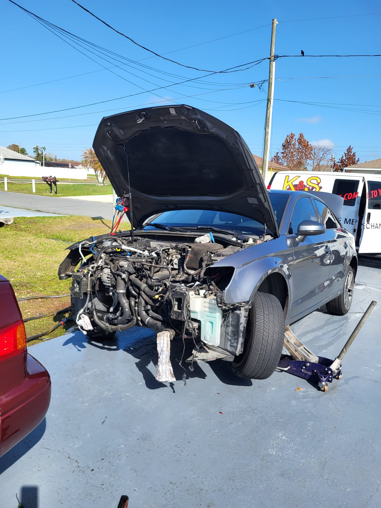 A car with the front bumper and engine bay exposed, K&S van parked behind