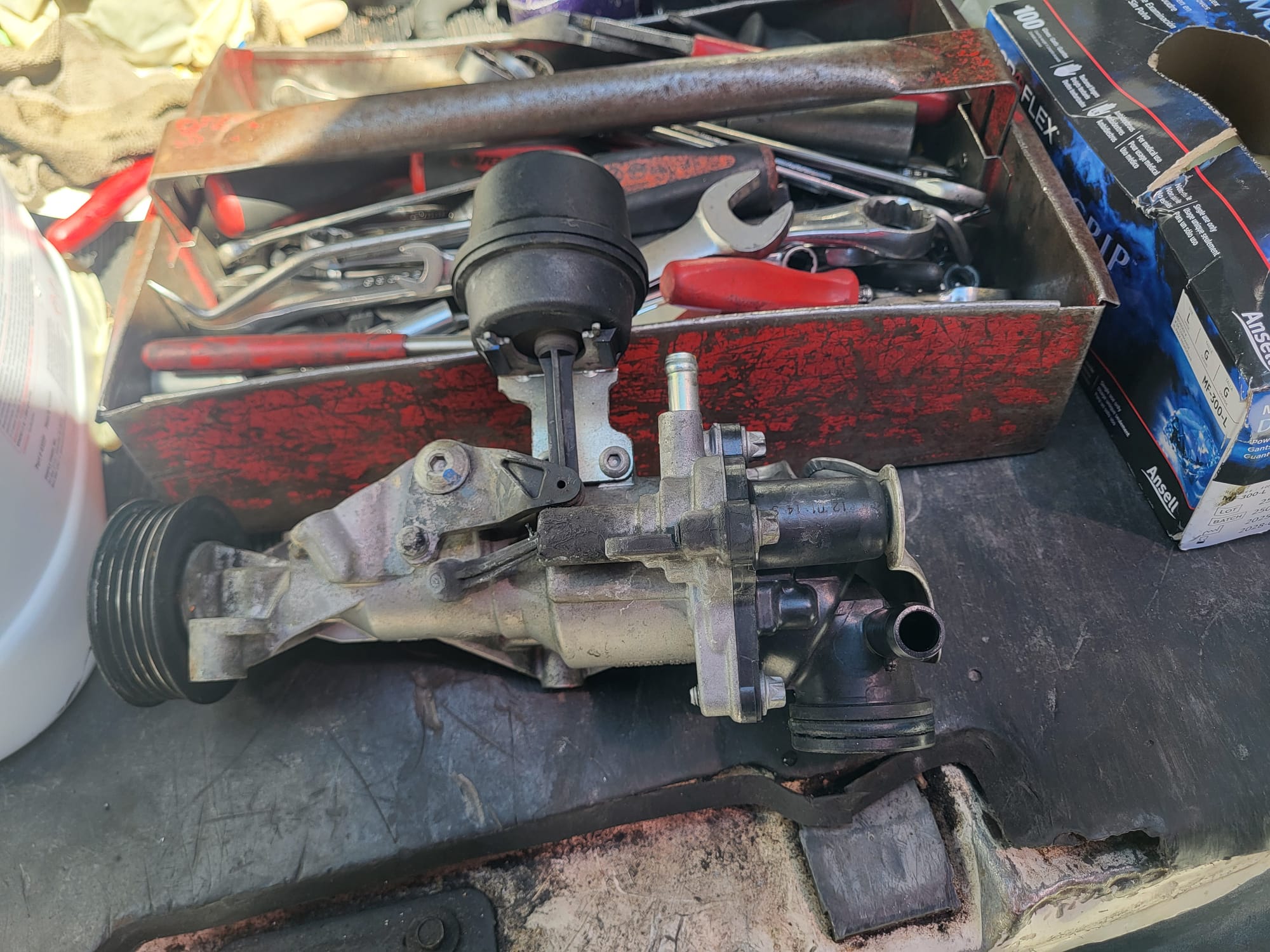 A removed engine component resting on a toolbox full of wrenches